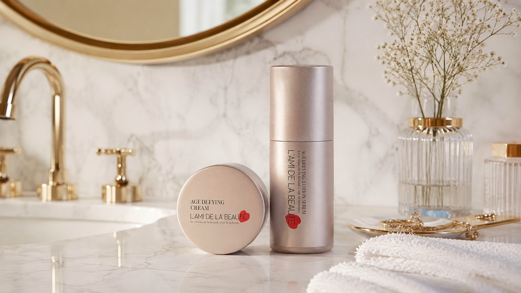 大理石の洗面台に置かれた「L'AMI DE LA BEAUTÉ」の2点セット。ゴールドの円柱ボトルの「エイジデファイング ローションセラム」と、その隣に並ぶ「エイジデファイング クリーム」。背景にはゴールドの蛇口、丸い鏡、繊細なかすみ草が飾られており、エレガントで温かみのある雰囲気を演出しています
